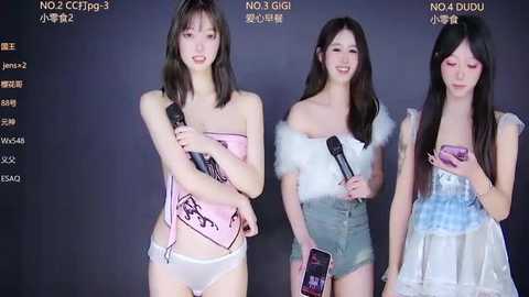 Video of three Asian women in revealing costumes holding microphones, smiling against a dark background, with Japanese text above.