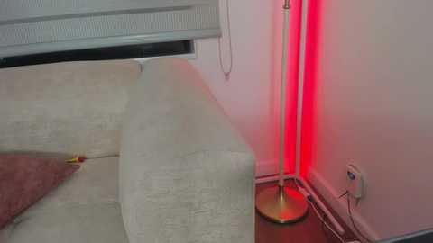 A video of a dimly lit room with a beige sofa, a red lamp, and a white electrical outlet on the wall.