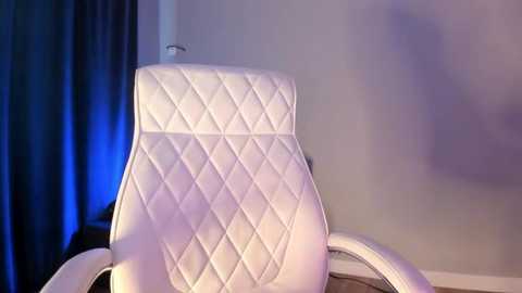 Video of a white, diamond-patterned leather recliner chair with armrests, set against a backdrop of light blue curtains and a neutral wall.