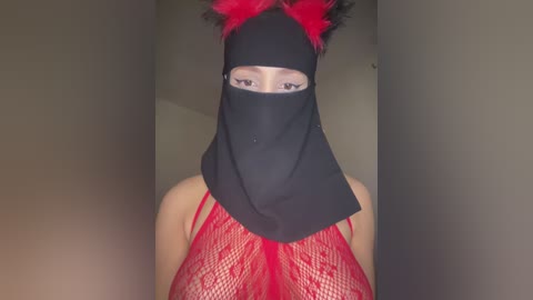 A video of a woman wearing a black burka with red lace lingerie visible underneath, standing in a dimly lit hallway.