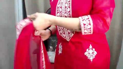 Video of a person wearing a vibrant pink salwar kameez with intricate white embroidery, holding a black umbrella, against a neutral background.