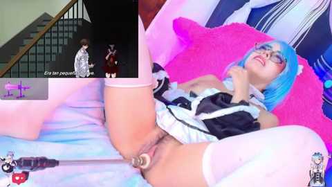 A video of a woman with blue hair, wearing a black maid outfit, lying on a bed with a pink pillow. She is visibly aroused, with her legs spread and a vibrator inserted into her vagina.