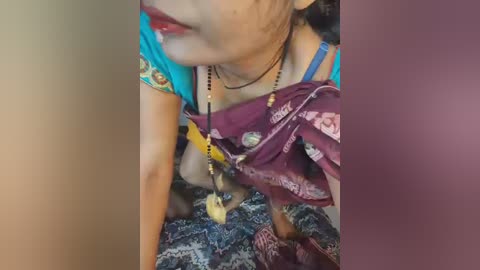 Video of an Indian woman with fair skin, wearing a blue blouse, purple saree, and gold jewelry, kneeling on a patterned floor.