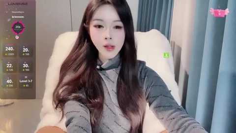 Media: Video of a young East Asian woman with long, straight black hair, wearing a gray sweater, sitting on a white chair in a modern room.