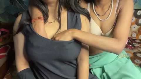 Video of two women, one with a large breast, wearing a dark blue tank top, and the other with a small breast, wearing a white bra and light green skirt.