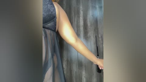 Video of a woman with fair skin, wearing a sheer black lace robe, adjusting her hair in front of a dark wood-paneled mirror.