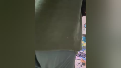 Video of a person's bare midriff, partially obscured by a light green curtain, with a colorful, cluttered background visible.