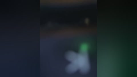 A blurry video featuring a green light source in the foreground, with a dark, indistinct background suggesting an urban or industrial setting. The image has a low-resolution and grainy quality.