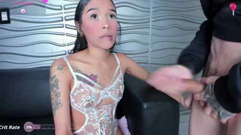 Video of a young Asian woman with wet hair, wearing a sheer, floral bodysuit, kneeling, with a man's erect penis in front of her.