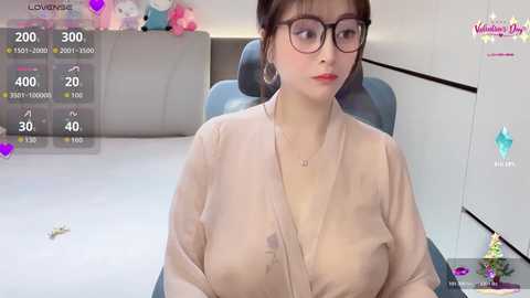 Video of a young Asian woman with glasses and red lipstick, wearing a low-cut beige blouse, sitting in a modern office setting with a grey chair and a white desk.
