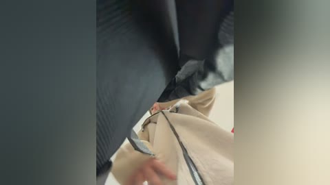 Video of two people in a dimly lit room; one person, with a dark jacket, is adjusting the beige coat of the other person, who appears to be wearing a grey sweater.