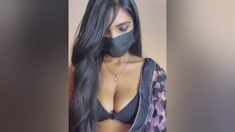 Video of a young woman with long black hair, wearing a black mask, black bra, and camo jacket.