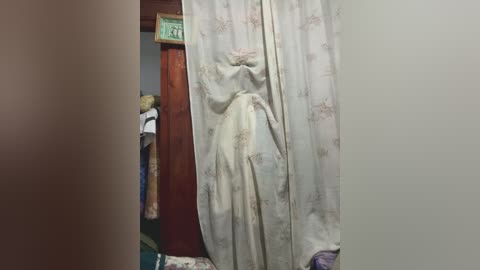 Video of a Victorian-style dress hanging on a door, featuring delicate lace and intricate embroidery. The dress is slightly open, revealing a delicate fabric lining. A green sign with numbers is partially visible above.