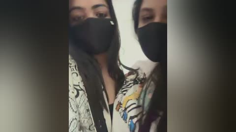 Media: Video of two women wearing black face masks, one with long dark hair, the other with a patterned shirt, against a blurred background.