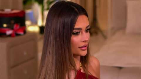 Video of Kim Kardashian in a red dress, with straight, long brown hair, wearing dark makeup, standing indoors near a blurred, beige-toned background.