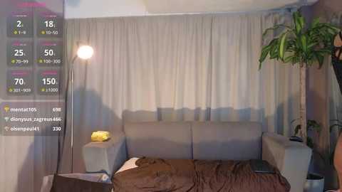 Media: Video of a modern living room with a gray sofa, beige curtains, potted plant, and yellow lamp. Digital screen overlay shows weather app with temperature and forecast.