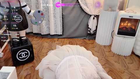 Video of a cozy living room with a white, fluffy rug, a white Chanel bag, a black controller, a white TV, and a fireplace.