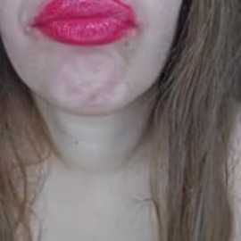 Close-up video of a woman with fair skin, wearing bright pink lipstick, and long, straight brown hair. Her lips are slightly puckered, and her shoulders are visible.