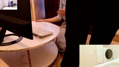 A video of a person in a white shirt, seated at a white round desk with a keyboard and monitor, viewed from the side, with a close-up of a white door with a round doorknob.