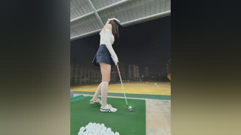 Media: Video of an Asian woman in a golf outfit, swinging a golf club on a green. Background features stadium seating and a nighttime cityscape.
