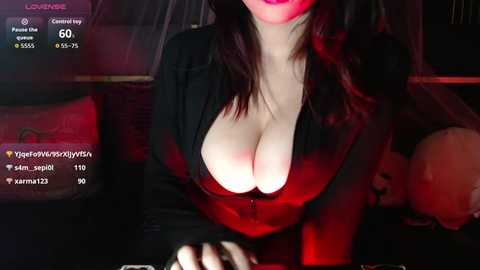Media: A video of a fair-skinned woman with dark hair, wearing a low-cut black top, in a dimly lit room, with a smartphone's camera viewfinder overlay showing her stats and comments.