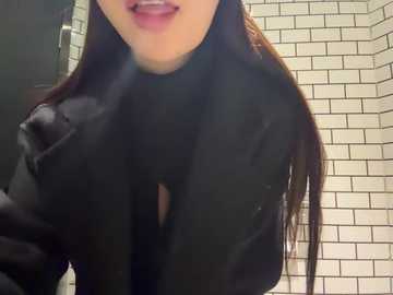 Video of a woman with long, straight brown hair, wearing a black, high-necked sweater. She has fair skin and light pink lips. Background shows white, subway-tiled walls and a dark door frame.