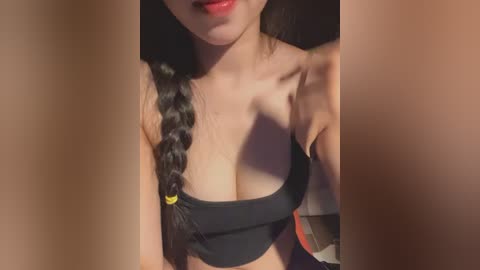 A close-up video of a woman with long black hair braided, wearing a black crop top, partially visible lips with red lipstick.