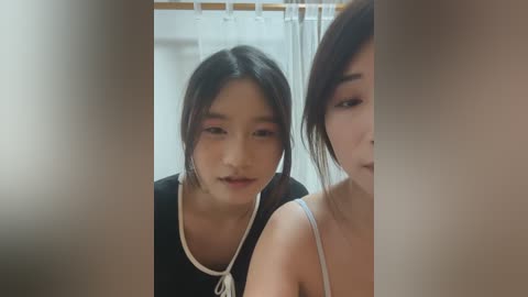 Video of two young East Asian women with pale skin, one with dark hair and the other with brown hair, standing in a bathroom, partially obscured by a shower curtain.
