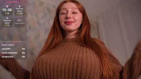 Video of a fair-skinned redhead woman with long hair, wearing a beige knitted sweater, smiling in a cozy room with a digital overlay of social media statistics.