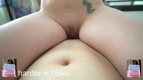 A close-up video of a woman's naked torso, showing her large, round buttocks and vulva, with a small tattoo on her right hip. The background is blurry.