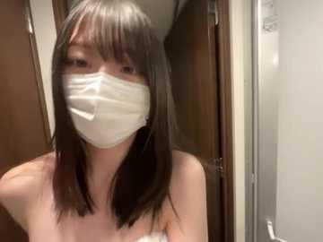 Video of an Asian woman with straight black hair and pale skin wearing a white face mask, standing indoors in a bathroom with wooden doors and a white sink.