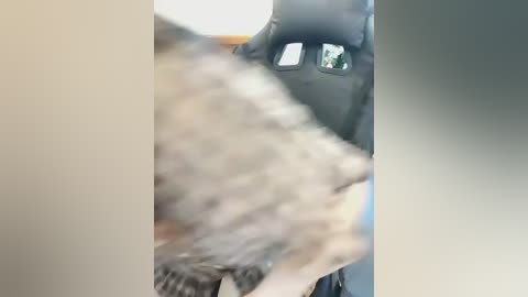 A blurred video showing a person in a black Batman costume with a reflective visor, standing beside a beige wall, with a furry, light-colored animal in the foreground.