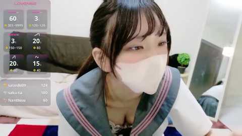 A video of an Asian woman with long black hair, wearing a school uniform with a white mask, indoors on a bed, with a smartphone screen displaying a countdown.