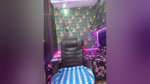 Video of a small, retro-style bedroom with floral wallpaper, a black leather chair, and a blue-patterned bedspread; purple accent lights add a modern touch.
