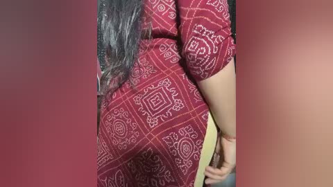 Video of a woman with long black hair, wearing a red patterned saree with intricate white designs, standing against a gradient background.