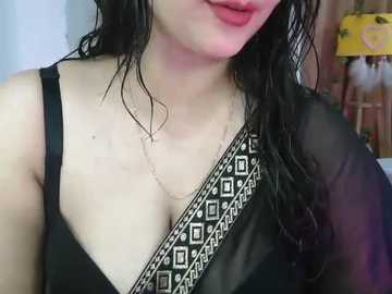 A close-up video of a woman with wet, dark hair, wearing a black top with a decorative black and white pattern, standing against a blurred background.