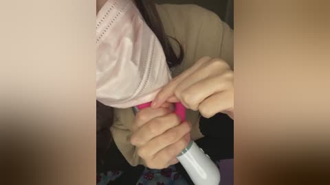 A close-up video of a person wearing a face mask, with a hand holding a pink and white hairdryer, focusing on the hand and mask, blurred background.