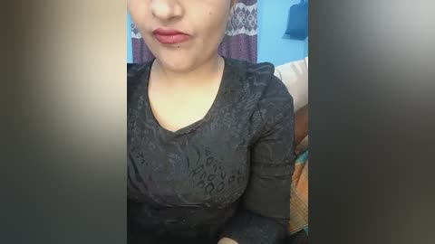 Video of a smiling woman with light skin, wearing a black lace top, in a room with a blue wall and patterned curtains.