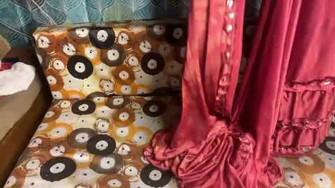 Video of a vintage-style sofa with a patterned fabric featuring circular faces in black, white, and brown hues, and a matching red curtain with ruffles. The background showcases teal, patterned wallpaper.