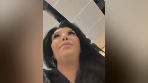 A video of a young woman with long black hair, wearing black makeup, and a black dress, taken from a low angle, emphasizing her upward gaze.