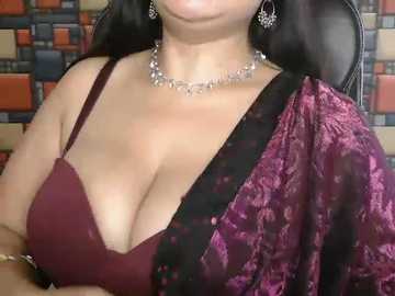 Video of a woman with long black hair, wearing a burgundy bra and a velvet sari with floral patterns. She has a silver necklace and earrings. Background features a mosaic tile wall.