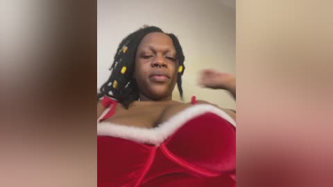A blurry video of a Black woman with medium skin tone, wearing a red velvet Santa outfit, with a visible nose ring, and black hair with yellow beads.