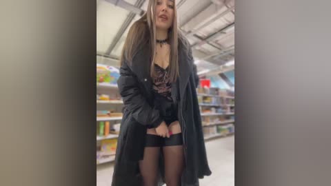 Video of a young woman with long, straight brown hair and pale skin, wearing a black coat, black lingerie, and thigh-high stockings in a supermarket aisle.