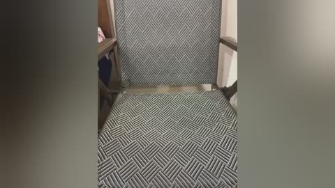 Video of a narrow hallway with a green and black zigzag-patterned carpet. On the left, there's a wooden shelf with a pink item. The walls are plain white.