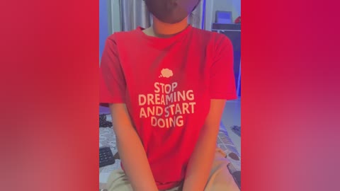 A video of a young person wearing a red T-shirt with the text \"STOP DREAMING AND START DOING\" in white letters. The background is a bedroom with a bed and a red gradient overlay.