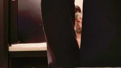 Video of a man's legs wearing dark pants, viewed from the side, with a blurred, partially visible face in the background.