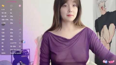 Video of a young East Asian woman with fair skin and long brown hair, wearing a sheer purple top revealing her bra, in a room with pastel-colored walls and a poster of a man with white hair.