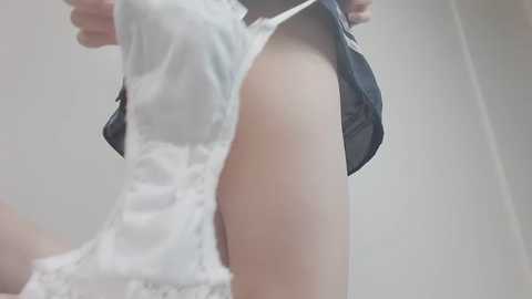 Video of a person wearing a sheer white lace dress, with a navy blue tie, showing their bare arm and side, taken indoors against a plain white background.