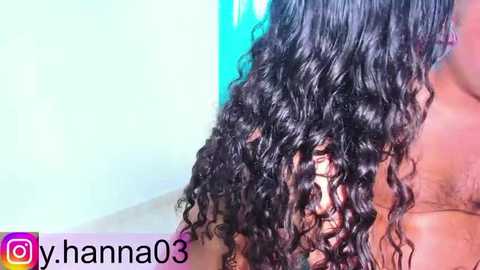 Video of a person with shoulder-length, curly black hair, partially wet, against a blurred, light blue background. Water droplets glisten on the hair. A watermark reads \"y_hanna03.\
