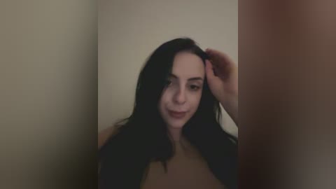 Media: A video of a young woman with long, dark hair, light skin, and a slim physique, standing in a dimly lit room. She wears a beige top and smiles slightly.